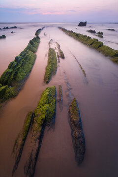 Dawn light softens the scene at Playa de Barrika, Bilbao, where moss-covered rock formations create a natural pathway into the sea