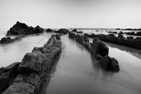 The textured rocks of Playa de Barrika stand stark against the smooth sea in this dramatic black and white coastal scene near Bilbao