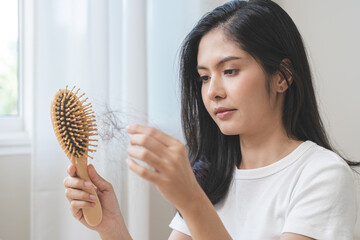 Serious asian young woman holding brush holding comb, hairbrush with fall black hair from scalp after brushing, looking on hand worry about balding. Health care, beauty treatment, hair loss problem.
