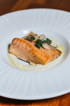 A beautifully poached salmon fillet rests on a creamy base, elegantly topped with caviar and fresh herbs on a white plate
