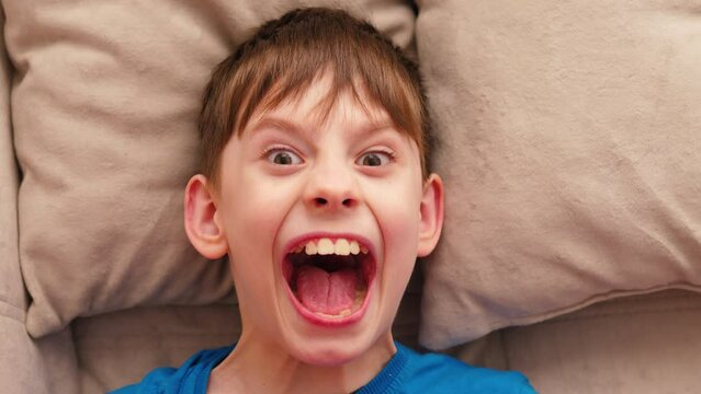portrait of a Caucasian boy 9 years old hiding under a blanket in fear, looking at the camera and screaming. childhood fears and phobias. teenage nightmare