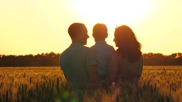 silhouette of a happy family at sunset. father and mother holding a little boy in their arms and kissing him. child and parents. dreams. family in a park. family in a wheat field