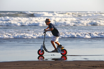 Guy riding gas powered scooter along the beach with big waves on the background