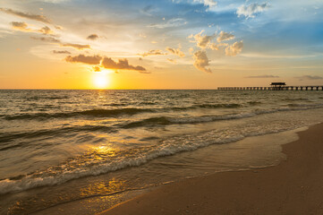 Fototapeta na wymiar Sandy beach with rolling waves and a distant pier at sunset. Naples Beach, Florida