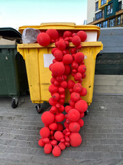 Red balloon garlands in a dumpster. Discarded used decoration. Concept of the melancholy after holiday party