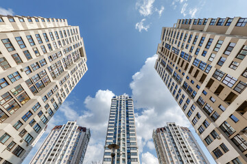 view from below into blue sky with clouds of large modern skyscraper residential complex with arch - obrazy, fototapety, plakaty
