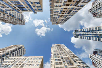 Fototapeta na wymiar view from below into blue sky with clouds of large modern skyscraper residential complex with arch