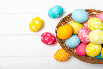 Easter basket filled with colorful eggs and a bouquet of tulips on a textured wooden table. Easter celebration concept. Colorful easter handmade decorated Easter eggs. Place for text. Copy space