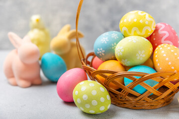Easter basket filled with colorful eggs and a bouquet of tulips on a textured wooden table. Easter celebration concept. Colorful easter handmade decorated Easter eggs. Place for text. Copy space