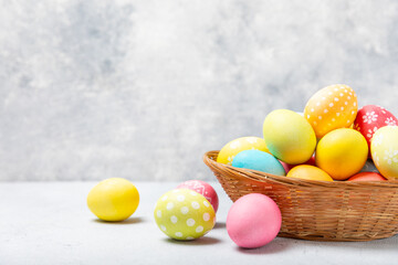 Easter basket filled with colorful eggs and a bouquet of tulips on a textured wooden table. Easter celebration concept. Colorful easter handmade decorated Easter eggs. Place for text. Copy space