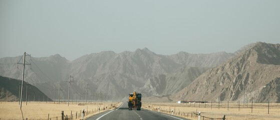 Image of a single tractor on the road in the middle of the yellow field and mountains. - Powered by Adobe