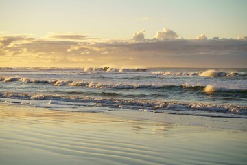 Breathtaking view of sea waves approaching the sandy beach during bright sunset