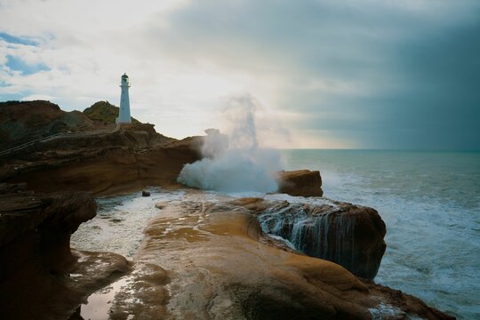 Scenic view of stormy breaking waves crashing against rock formations and Castlepoint Lighthouse