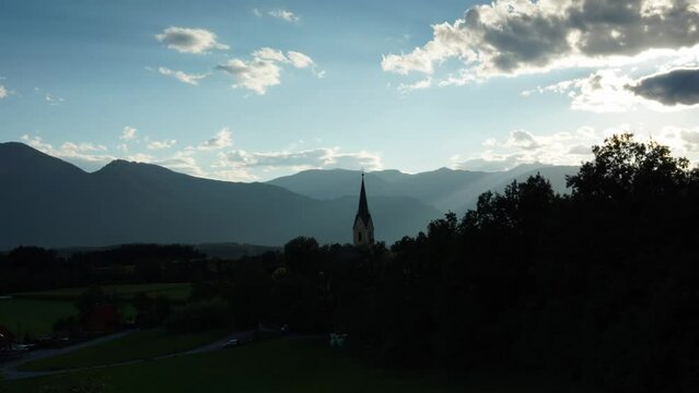 Timelapse of a church bell tower in the village with the sunset and mountains in the background