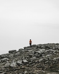 Vertical shot of a person standing on the top of the rocky mountain on a foggy day