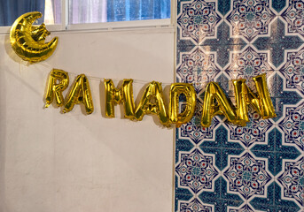 Golden words RAMADAN made of inflatable balloons, on a wall. Gold foil balloon letters