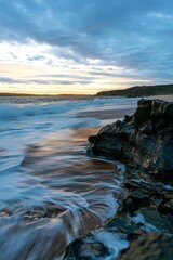 Vertical shot of a sea with waves approaching the cliffs of the beach and the sunset on the horizon