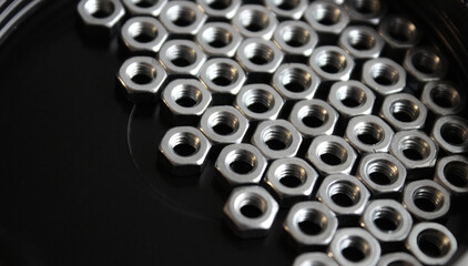 Heavy hex nuts on a black flat surface are huddled together on the right side of the image