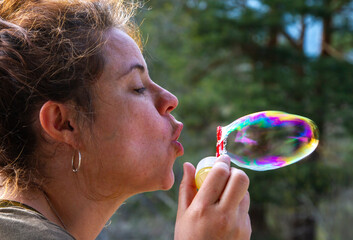 A pretty young woman plays with blowing soap bubbles on a sunny day
