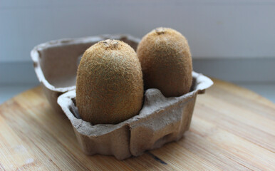 Pair of ripe juicy kiwifruits in a craft tray on a wooden board top view
