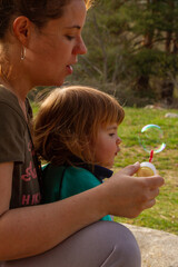 A pretty young woman plays with her two-year-old daughter to blow soap bubbles on a sunny day
