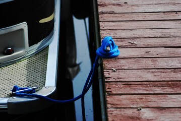 Selective closeup focus of a small boat tied to a wooden dock with a blue rope