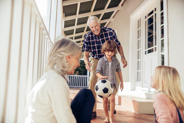 Grandparents and grandchildren having fun with a soccer ball on house porch