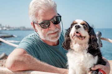 Portrait of old attractive senior bearded man sitting close to the sea with his cavalier king charles dog. Best friend forever concept. Horizon over water - obrazy, fototapety, plakaty