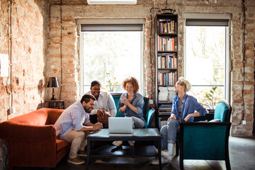 Happy diverse team in a meeting at a creative office space with a laptop