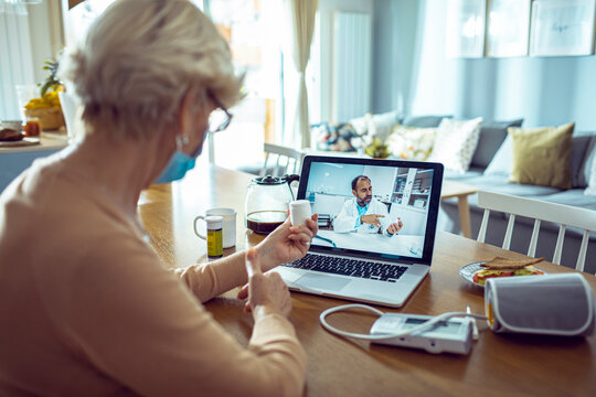 Elderly woman in telehealth session with doctor on laptop at home