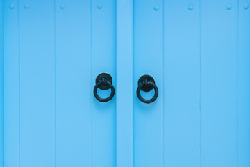 Blue-painted vintage wooden door with metal handles close up. Cycladic architecture in Santorini island, Greece.