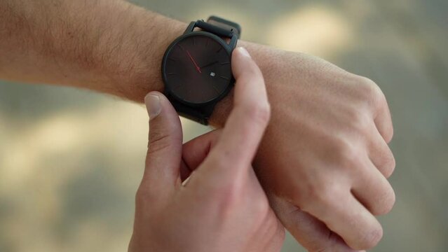 A Caucasian man looks at his wristwatch on the street. Closeup of watch on arm