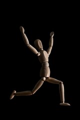 Vertical closeup of a wooden marionette figure dancing against a black background