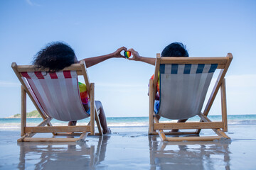 LGBTQ couple lover sitting on beach chair pose happiness show heart rainbow color on beach in...