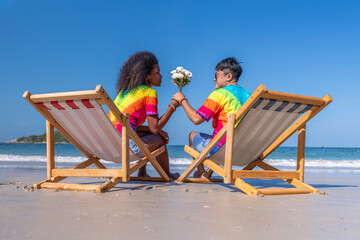 Romantic happiness couple LGBTQ lover sitting on beach chair giving flower show happiness with equality freedom of love friendship and LGBTQ couple is relax summer holidays concept. - obrazy, fototapety, plakaty