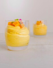 Vertical closeup of mango puddings served in glasses on a white background