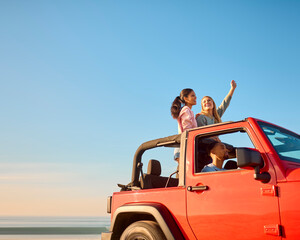 Couple With Friends On Vacation Driving Car On Road Trip Adventure To Beach Standing Up Through Roof