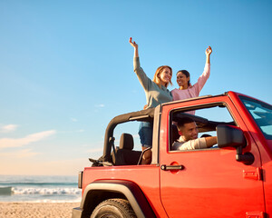 Couple With Friends On Vacation Driving Car On Road Trip Adventure To Beach Standing Up Through Roof