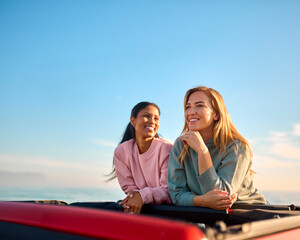 Two Women On Vacation In Car Driving On Road Trip Adventure To Beach Standing Up Through Roof