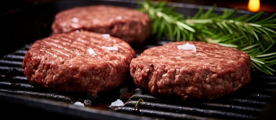 Three juicy hamburger patties are sizzling on a hot grill alongside a fresh sprig of rosemary, creating a mouthwatering aroma