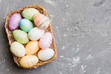 Colorful Easter eggs in wicker basket against colored background, closeup. top view with copy space