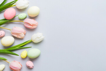 Happy Easter composition. Easter eggs on colored table with yellow Tulips. Natural dyed colorful eggs background top view with copy space