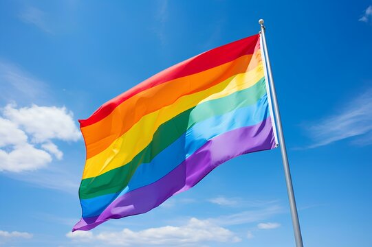 Close-up of a vibrant LGBTQ rainbow flag waving proudly against a clear blue sky, symbolizing freedom and unity.
