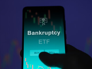 An investor analyzing the bankruptcy etf fund on a screen. A phone shows the prices of Bankruptcy