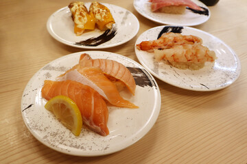 many dishes of delicious Japanese sushi such as , tuna, shrimp , salmon, are on the wooden table in the conveyor belt sushi shop at fish market in Japan