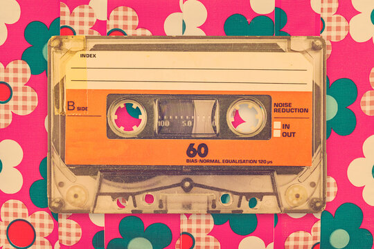 Vintage orange audio compact cassette in front of a background with flower pattern