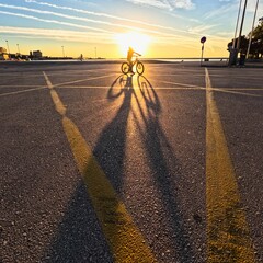 Man riding a bike with long shadows of setting sun in Patras port