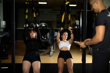 Intense gym training with women performing TRX exercise.