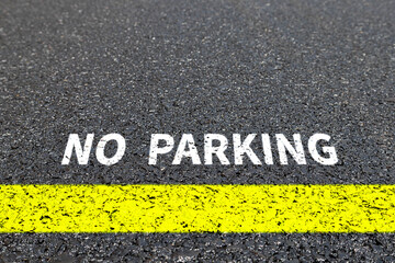 NO PARKING signage on asphalt road floor. NO PARKING on the road. Yellow line.