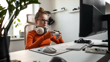 Teenage girl is sitting in a comfortable computer chair, holding a white gamepad in her hands and...